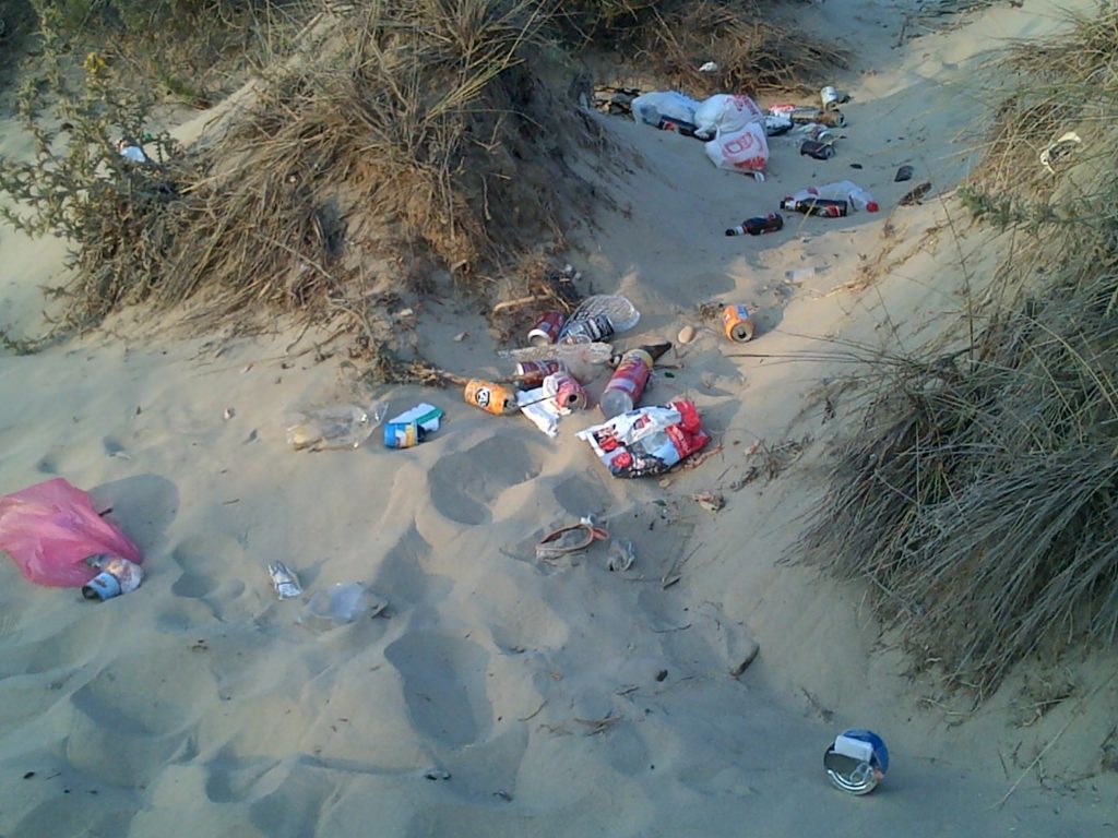 Playa ensuciada con lata y plásticos en el mar