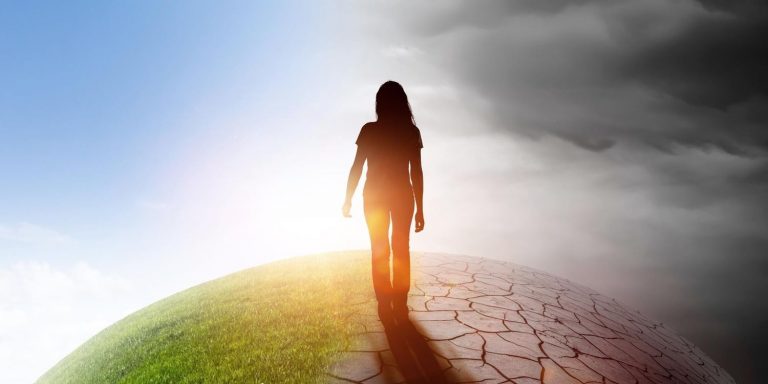 Imagen de una mujer de espaldas al contraluz mirando media Tierra seca y media verde, haciendo referencia al cambio climático.