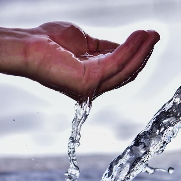 Foto de un chorro de agua y una mano sosteniendo el líquido.