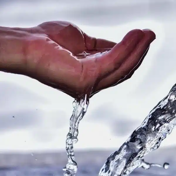 Frenar el cambio climático: ¿Cómo hacerlo posible? ¿Estás buscando reducir tu huella de carbono? ¿Eres de esas personas que les preocupa el calentamiento global? ¿Quieres pasar a la acción? ¿Quieres saber qué puedes hacer tú ante la crisis climática? Mira estas 10 formas de frenar el cambio climático. Foto de un chorro de agua y una mano sosteniendo el líquido.