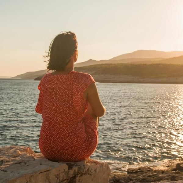 Foto de una mujer de espalda mirando al mar y a la tierra. Mujer reflexionando.