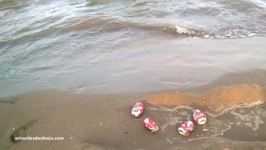 Foto de 4 latas tiradas en la playa junto al mar.