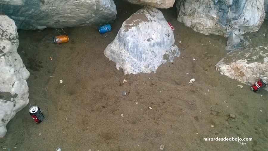 Foto de un rincón rocoso de una playa llena de basura con lastas de aluminio. Ejemplo de imágenes del mar contaminado.