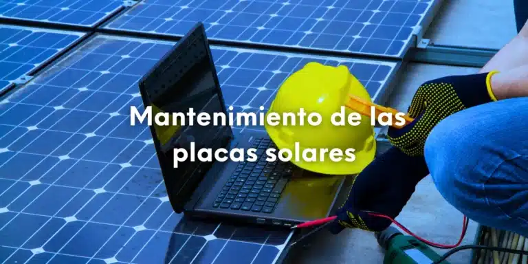 Foto de un técnico con un portátil y casco de obras apoyado sobre unas placas solares a las que está haciendo el mantenimiento.